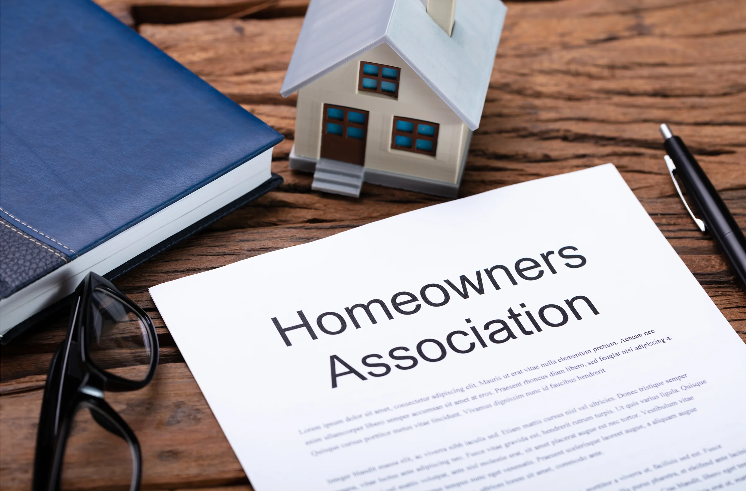 Rectangle 1152 Homeowners Association document on a table with a model house, pen, glasses, and a blue book.