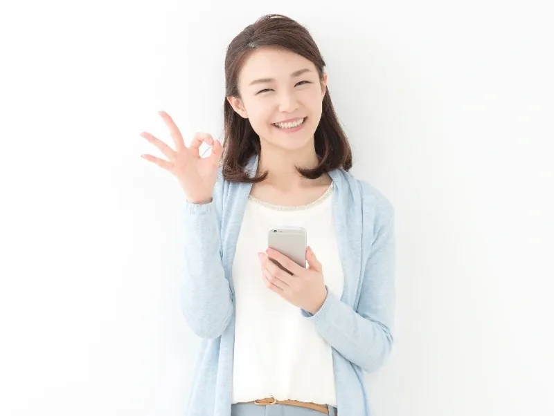 A woman holding her phone and making an ok sign.